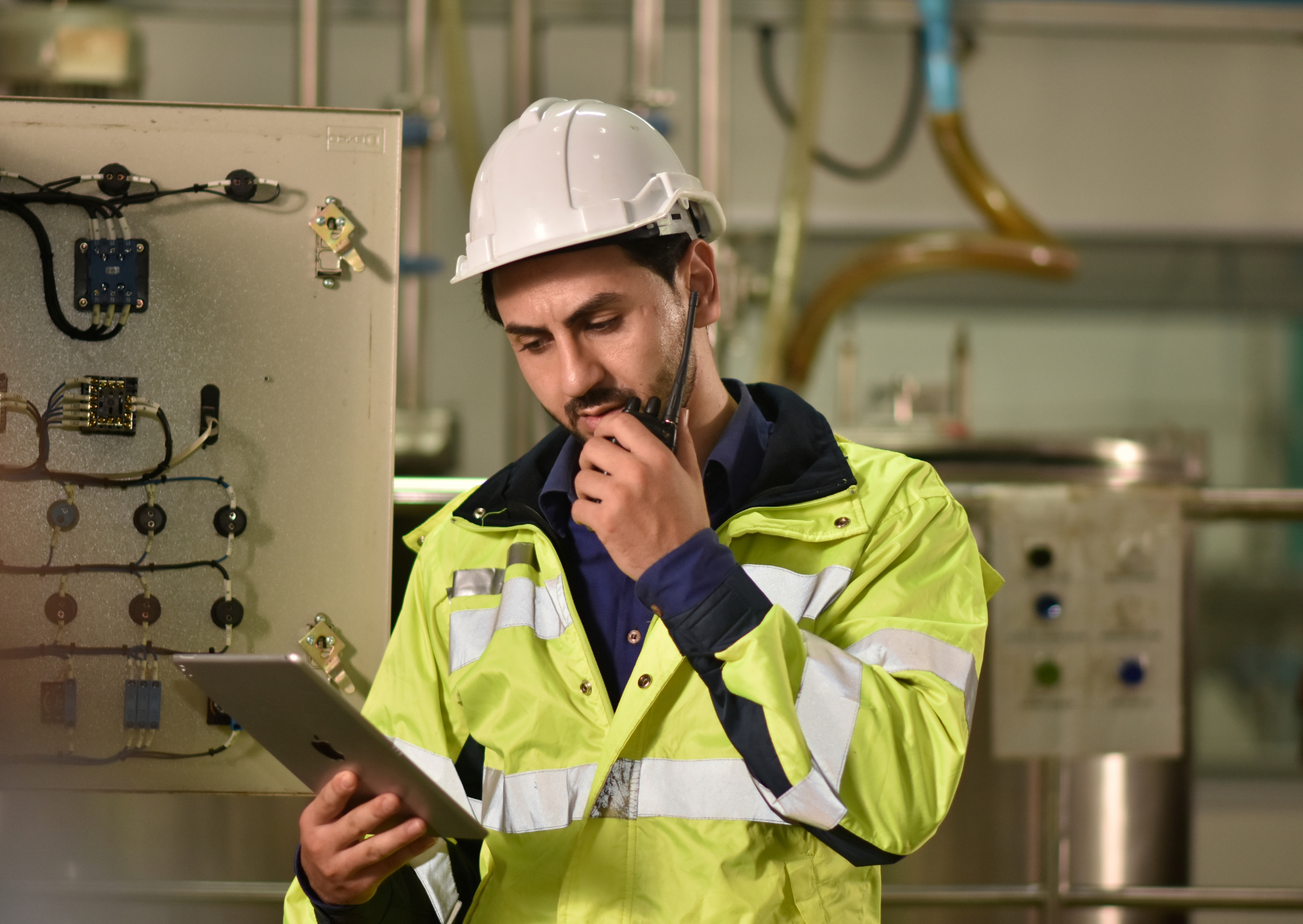Een man in een veiligheidsvest gebruikt een tablet terwijl hij naar de omgeving kijkt.