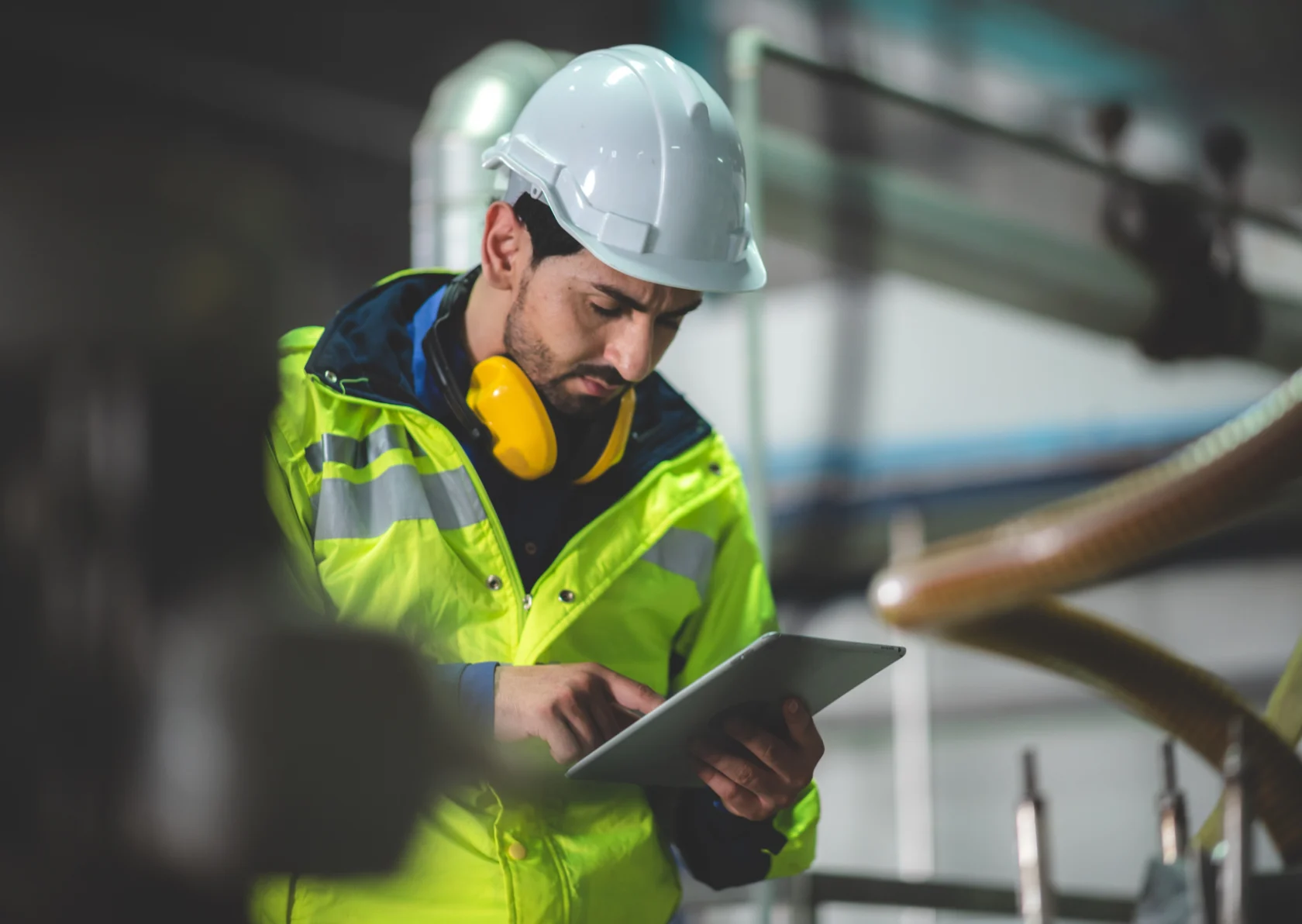 Een man met een veiligheidsvest en hardhat bekijkt informatie op een tablet.