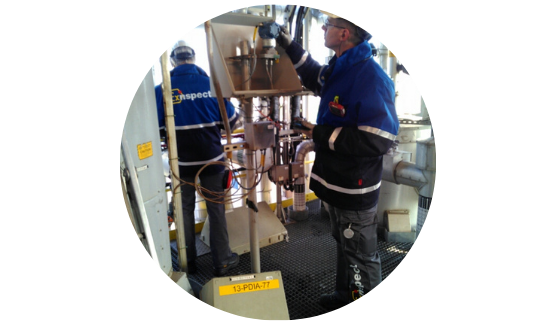 Twee mannen in blauwe jassen van ExInspect werken samen aan een machine in een industriële omgeving.